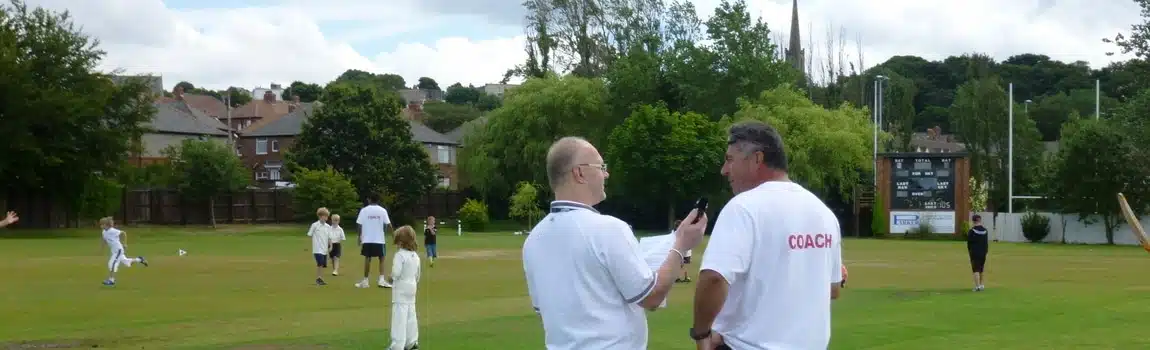 Cricket coach speaking with a player during a 1-to-1 cricket coaching session on an outdoor field