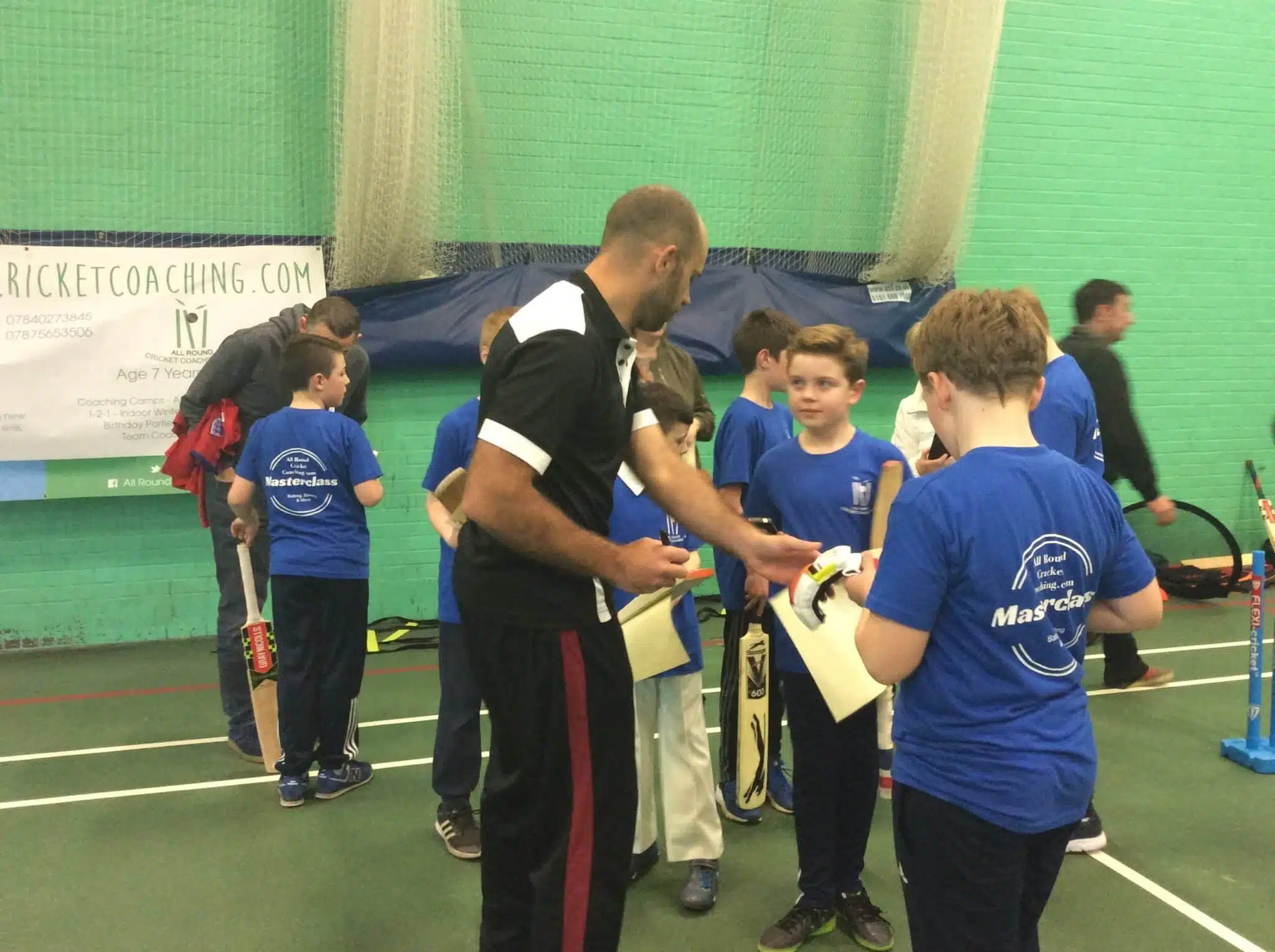 Coach leading a group of young players during a school holiday cricket coaching session in indoor nets
